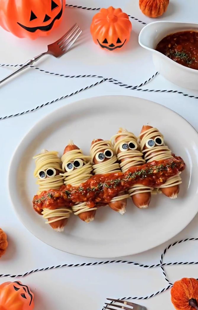 a white plate topped with pasta covered in googly eyes next to two pumpkins