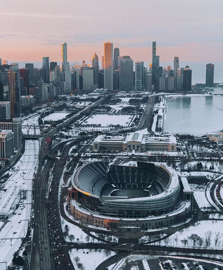 an aerial view of a stadium in the winter with snow on the ground and large city buildings