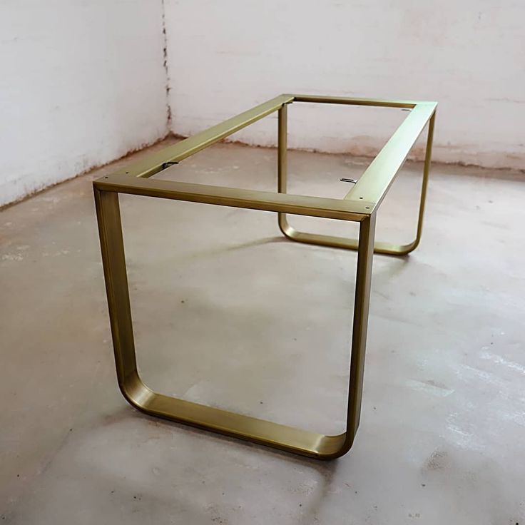 a gold metal table sitting on top of a cement floor next to a white wall