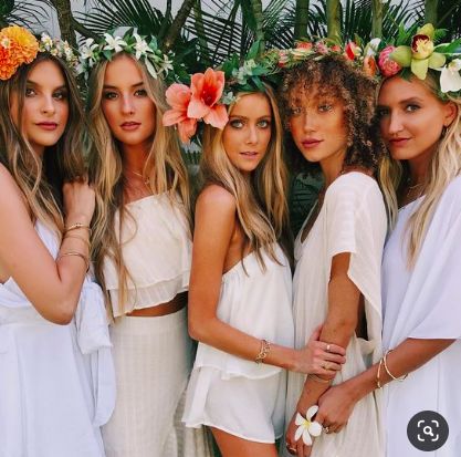 four beautiful women standing next to each other in white dresses and flower crowns on their heads