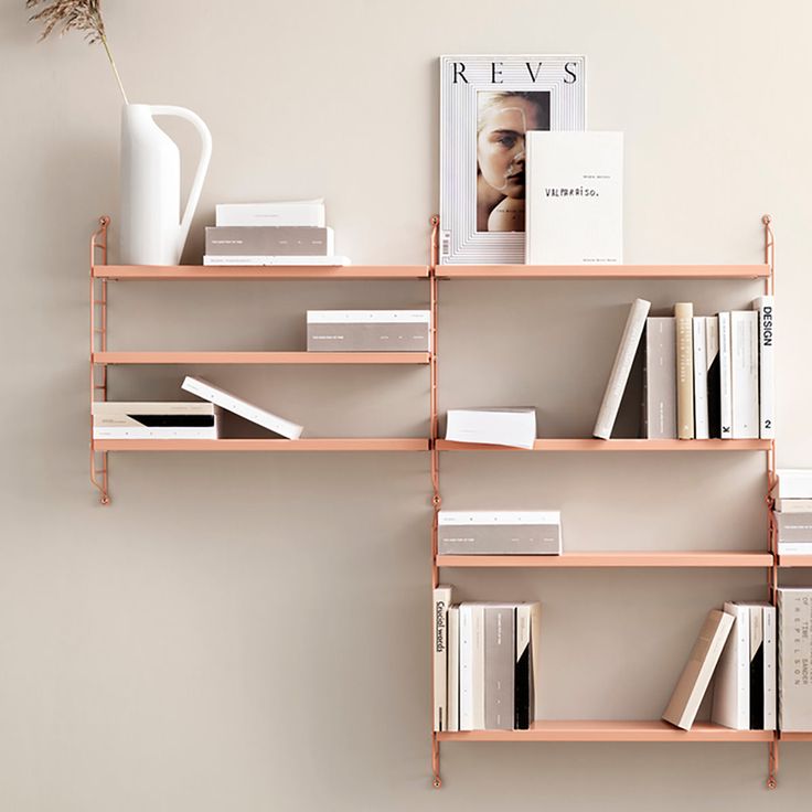 a shelf with books, magazines and a vase on it next to a white wall