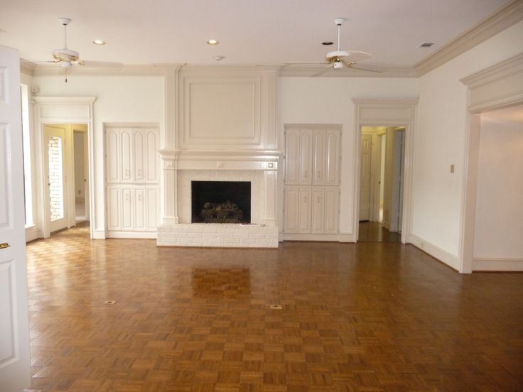 an empty living room with hard wood floors and white cabinetry on either side of the fireplace