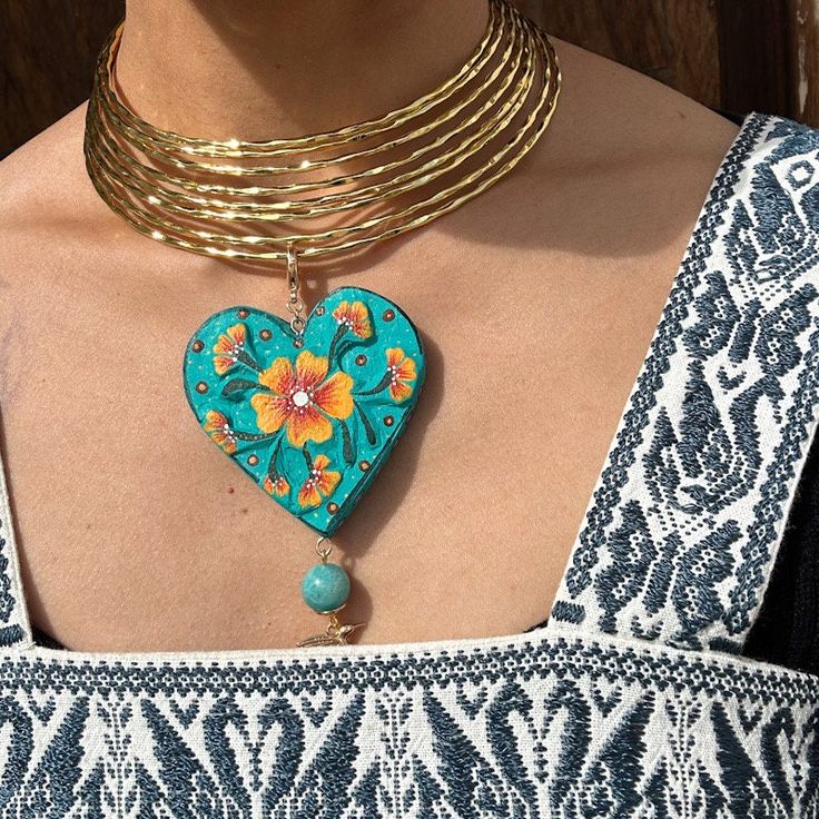 We combine art and elegance to create this beautiful piece. Our handmade necklaces will be the perfect element to make your outfit standout. You could have the entire collection or gift them to someone special.  Material: Real Gold plate brass, copal wood Dimensions: heart 6cm, charm length 11cm Features : Lightweight, Unique and Simple design The Talavera of Puebla is part of the intangible heritage of humanity, declared by UNESCO. It is a type of majolica ceramic with a mixture of Chinese, Italian, Spanish, and indigenous techniques, and its colors are obtained from natural pigments. Its main characteristics are its vitreous finish and the use of bulky cobalt blue, this made it even more exclusive and ostentatious than Spanish craftsmanship. Its production requires at least 120 hours of Unique Festival Necklaces With Round Pendant, Unique Festival Jewelry With Clavicle Chain, Bohemian Gold Plated Jewelry For Festivals, Gold Dangle Jewelry With Artistic Design, Artisan Gold Necklace With Round Pendant, Long Clavicle Chain Choker As A Gift, Unique Gold Heart Pendant Jewelry, Handmade Artisan Gold Custom Necklace, Bohemian Pendant Necklace With Unique Design