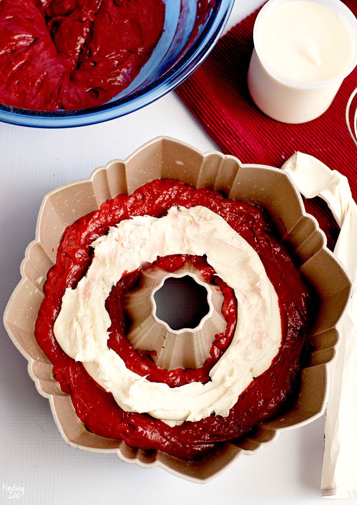 a red cake with white frosting in a pan next to a whisk