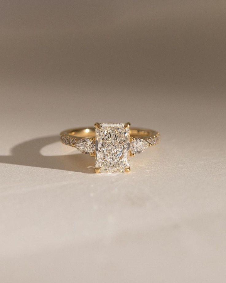 a yellow gold ring with a square cut diamond in the center and two smaller diamonds on each side