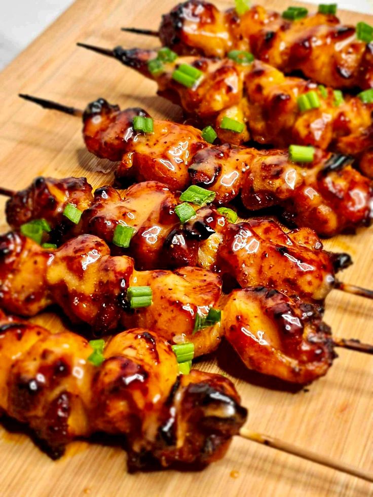 several skewers of chicken are lined up on a cutting board with green onions