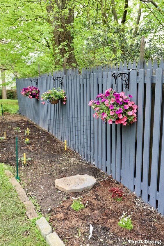 some flowers are hanging on the side of a fence with a garden bed in front