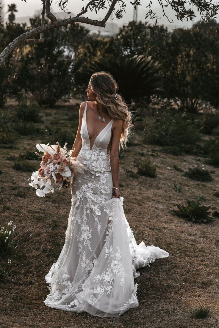 a woman in a wedding dress is walking through the grass with flowers on her bouquet