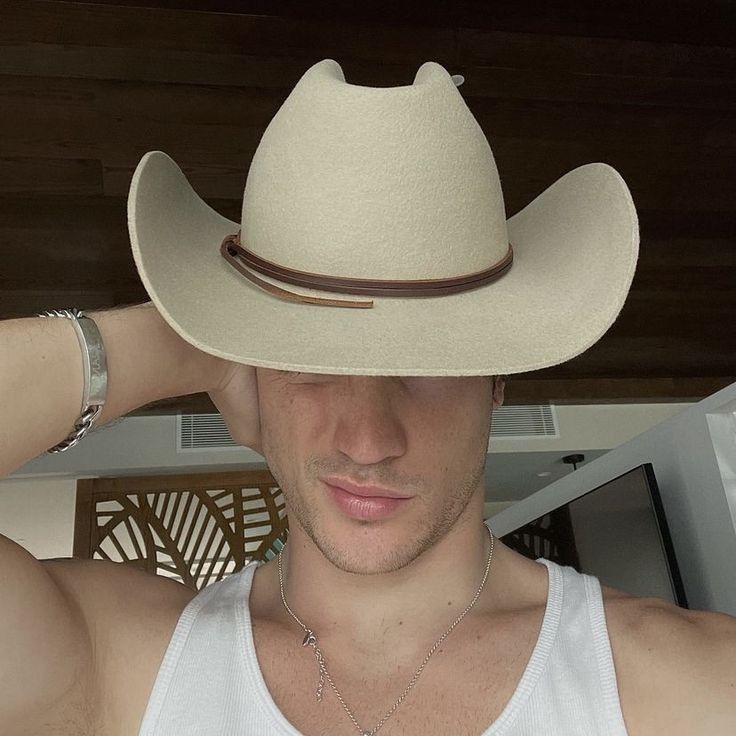 a man wearing a white tank top and a cowboy hat