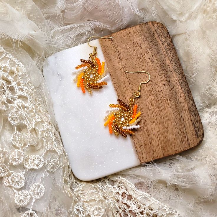 a pair of orange and white earrings sitting on top of a piece of wood next to lace