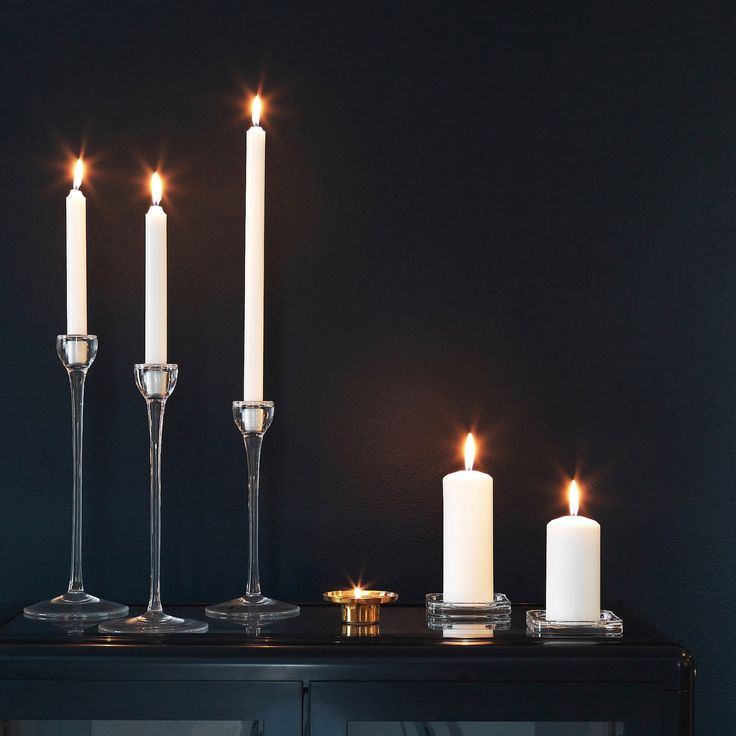 three candles are lit on a black table with two wine glasses and one candle holder