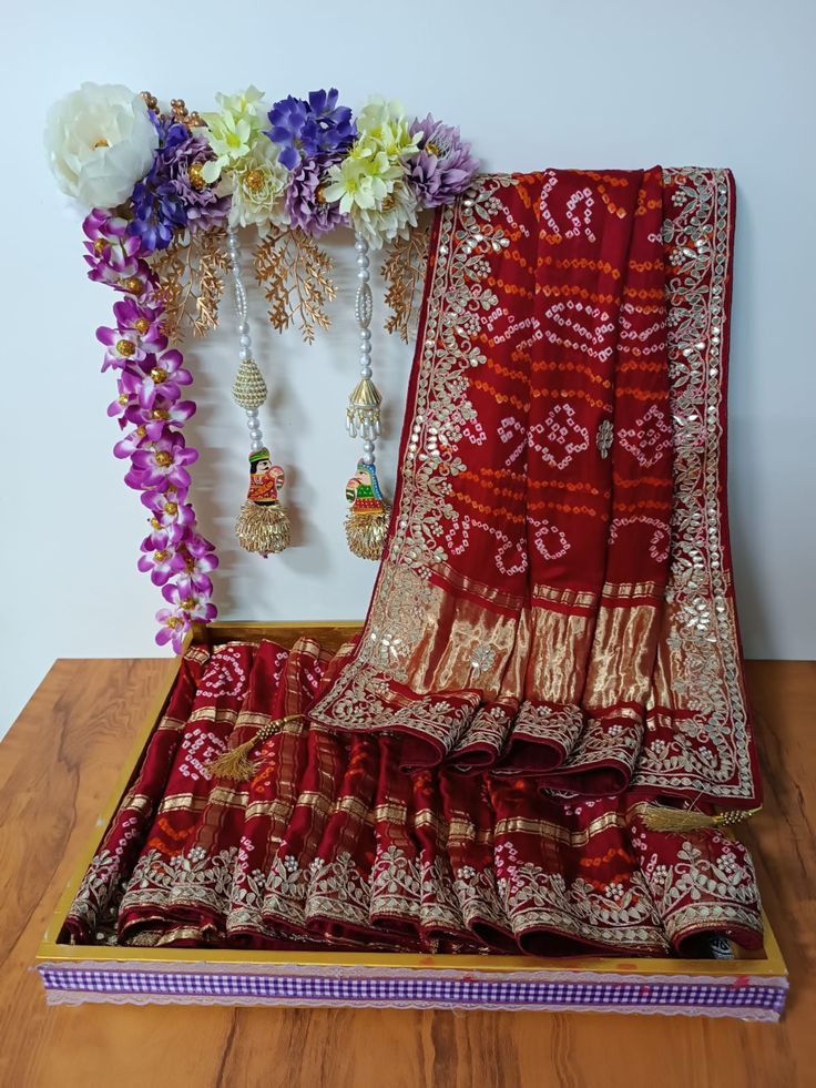 a red and gold sari with flowers on the wall next to it is sitting on a wooden table