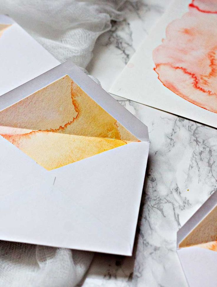 three envelopes with watercolor designs on them sitting on a marble counter top next to each other