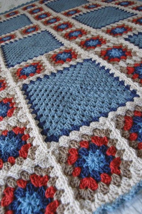 a crocheted blanket with blue, red and white squares on it sitting on a bed