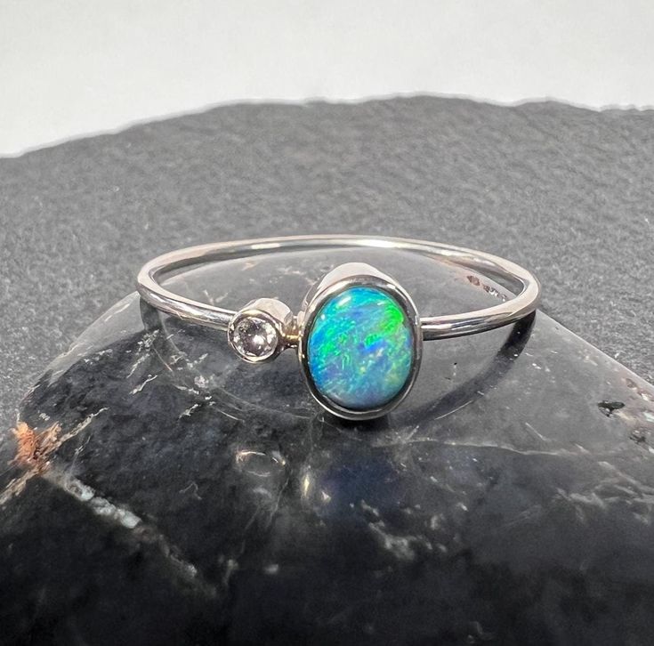 Australian black opal with natural diamond accent stacker ring set in 14k white gold. 14k white gold opal stacker ring. Cute little itty bitty 5.3mm x 4.25mm .38 carat Australian black opal from Lightning Ridge. 1.9mm natural G/H SI diamond .027 carat. 14k white gold (not rhodium plated) band and bezels. 1mm round solid 14k white gold band. Currently US size 8 for scale (select size at checkout). Hand made, one of kind All of our creations are made out of 14K Gold (Yellow, White, Rose) or 925 Sterling Silver, None are filled or electroplated.  All of our stones are Nature-made, therefore some natural flaws may be present. Hand crafted in the We Work Gems Shop in Washington State. Size and weight are approximate. Please feel free to ask any questions. Back to our shop https://www.etsy.com/s Black Opal Jewelry Rings, Opal And Black Diamond Ring, Black Opal Diamond Ring, Black Australian Opal Ring, Black Opal Ring Opal Auctions, Elegant Silver Opal Stackable Rings, Silver Opal Dainty Rings, Oval Opal Stackable Jewelry, White Gold Opal Jewelry With Birthstone