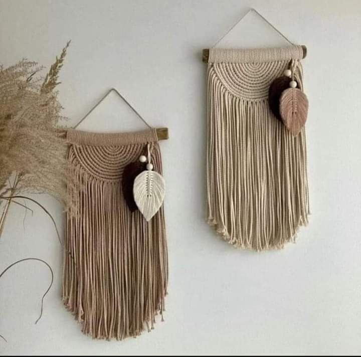 two wall hangings with tassels and leaves on them, one holding a plant