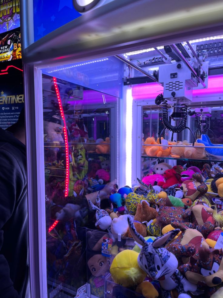 a man looking at stuffed animals in a toy store display case with neon lights behind him