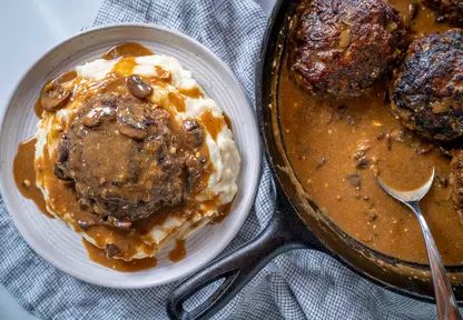 two meatballs and mashed potatoes in a skillet with gravy on the side