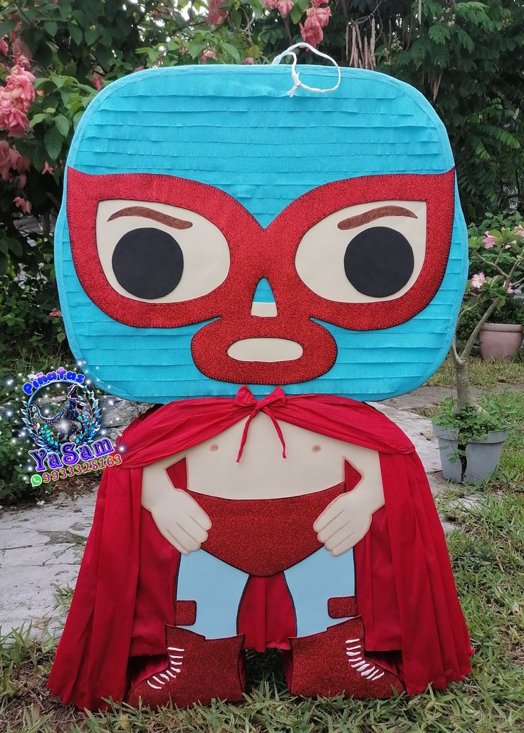 a cardboard cut out of a person wearing a red cape and blue mask, sitting in the grass