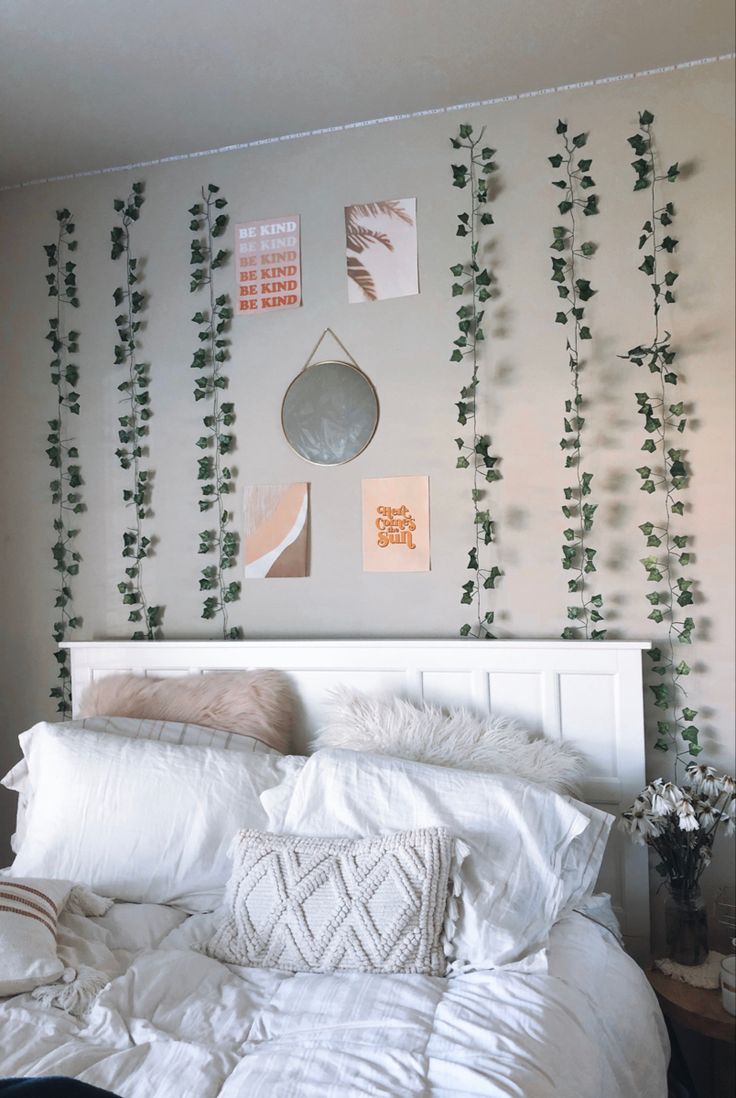 a white bed topped with lots of pillows next to a wall covered in green plants