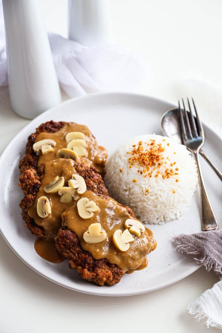 a white plate topped with meat covered in gravy next to rice and a fork