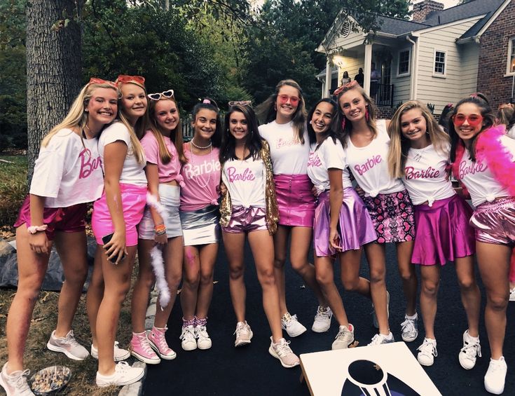 a group of young women standing next to each other in front of a house with pink and white shirts