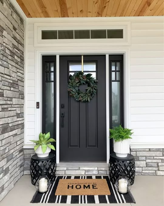 a black front door with a welcome mat and potted plants