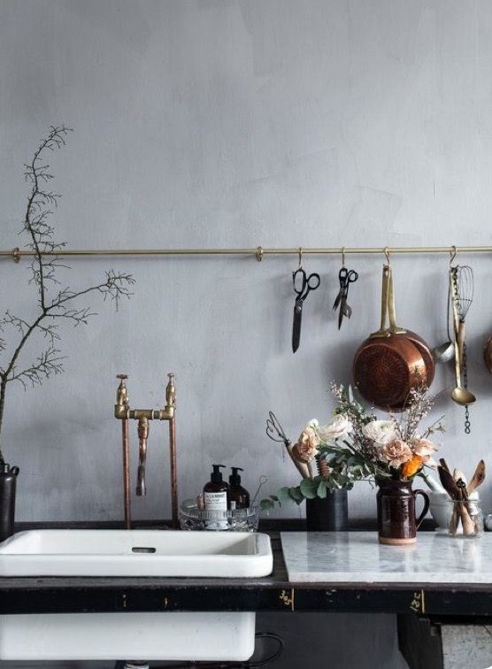 pots and pans are hanging on the wall next to a sink with flowers in it