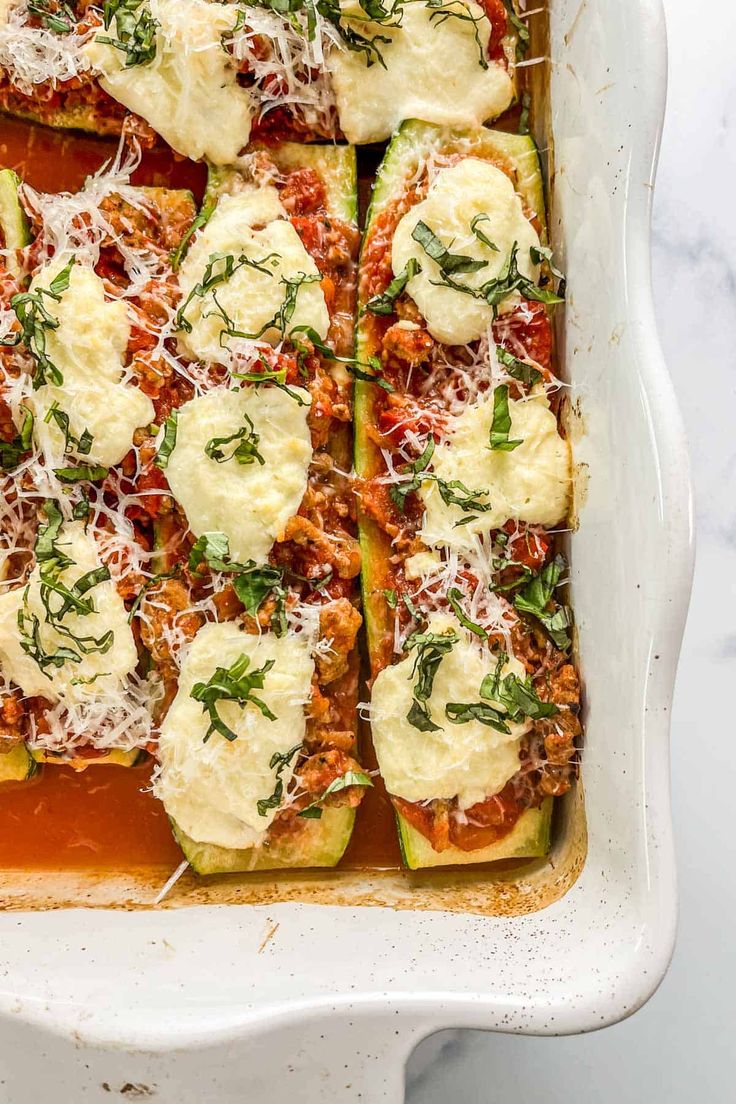 stuffed zucchini boats in a white casserole dish topped with cheese and herbs