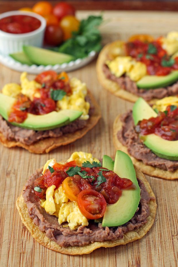 some food is laying out on a cutting board with tomatoes and avocado in the background