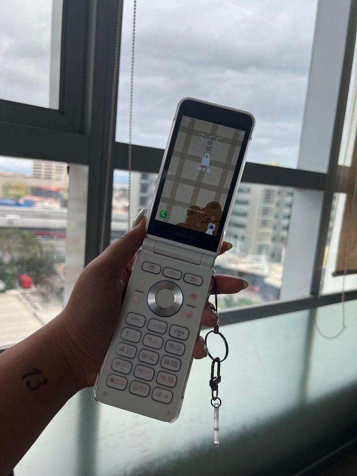 a person holding up a cell phone in front of a window with a keychain