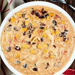 a white bowl filled with corn and black olives next to a red napkin on top of a wooden table