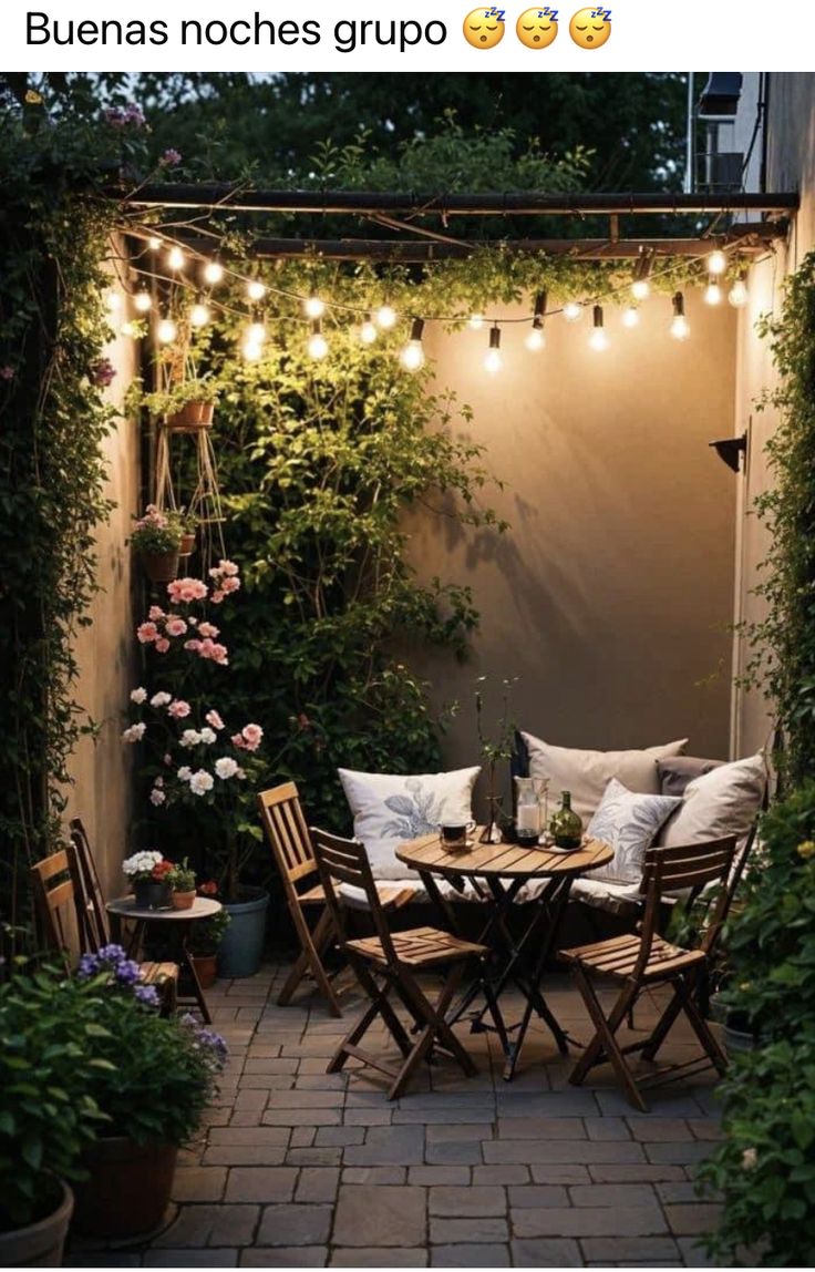 an outdoor dining area with lights strung over the table and chairs, surrounded by greenery