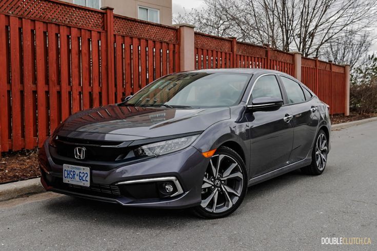 a gray honda civic is parked in front of a red fence