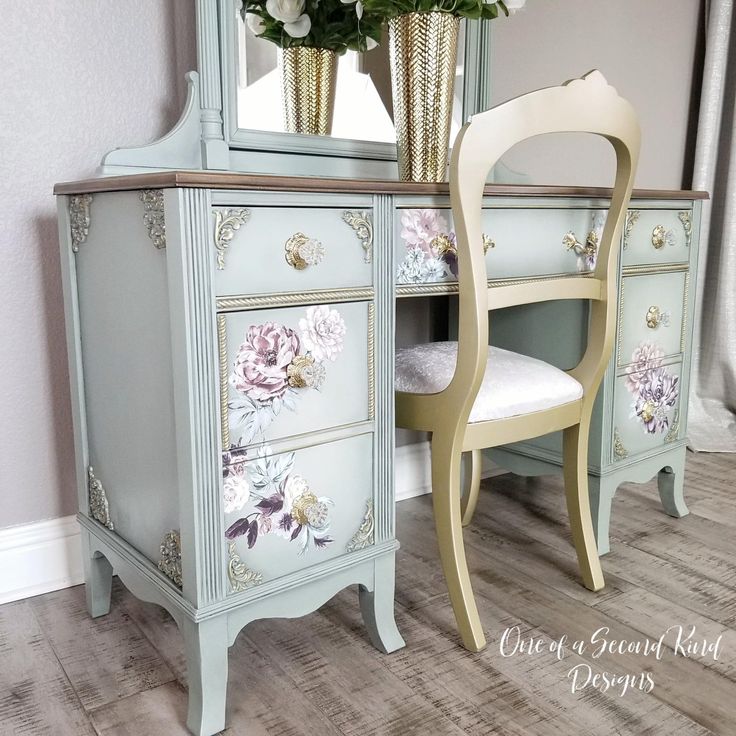 a white chair sitting next to a blue dresser with flowers on it's drawers