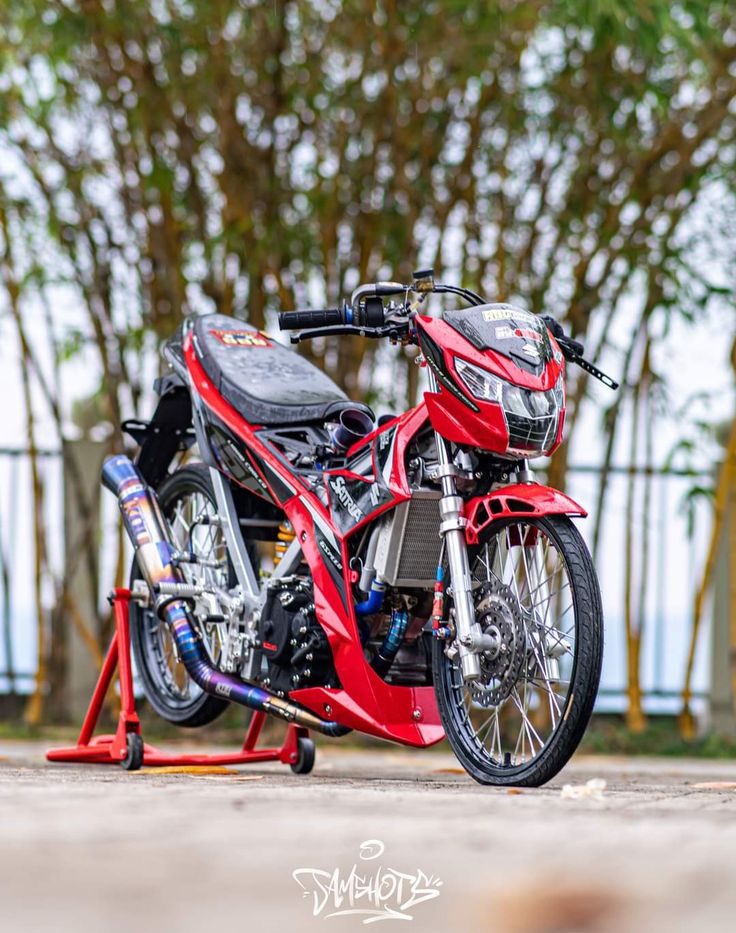 a red motorcycle parked on top of a street next to a tree filled parking lot