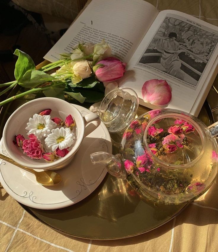 a tea pot filled with flowers on top of a table next to an open book