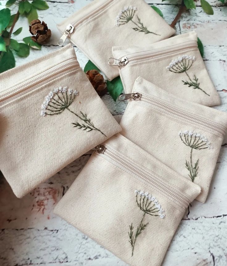 four small zippered pouches with embroidered flowers on them and pine cones in the background