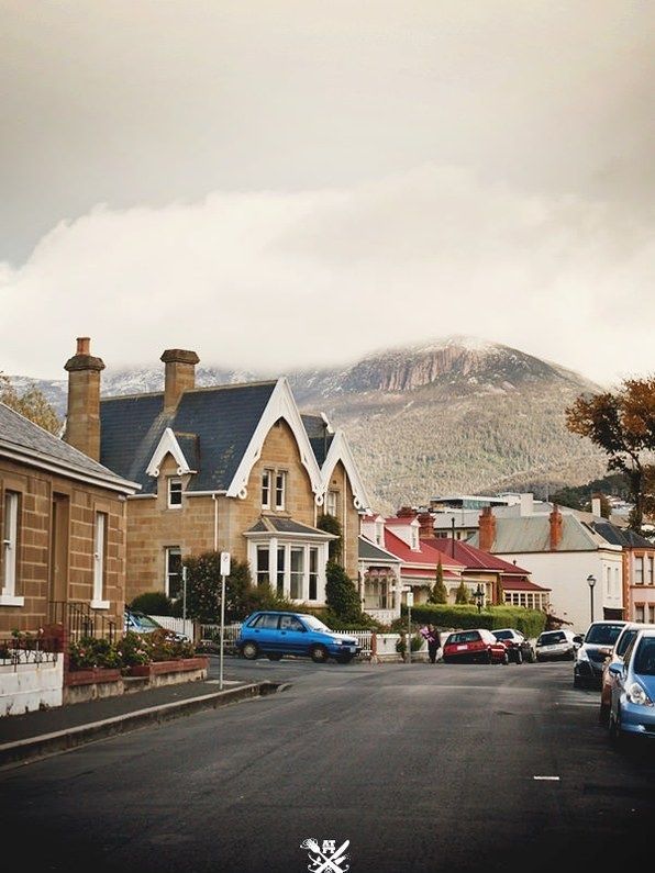 cars are parked on the street in front of some houses and mountain range behind them