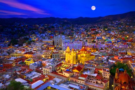 an aerial view of a city at night with the moon in the sky above it