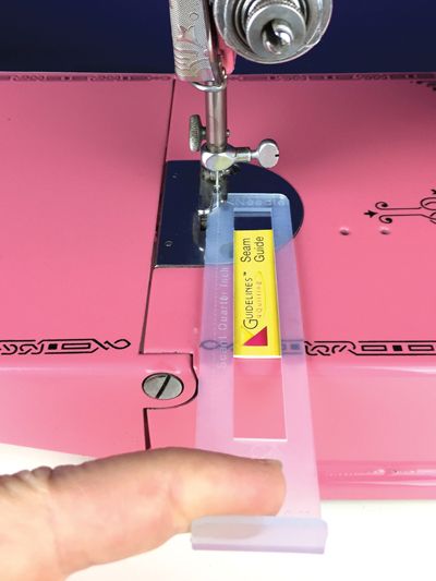 a person is using a sewing machine to sew something on the pink sheet that they are holding in their hand