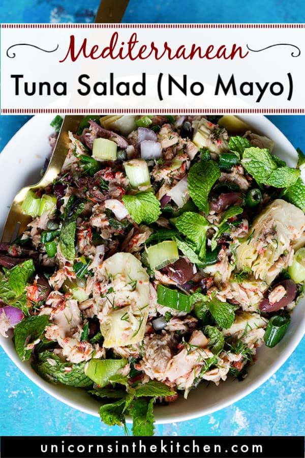 a white bowl filled with tuna salad next to a spoon and blue table cloth in the background