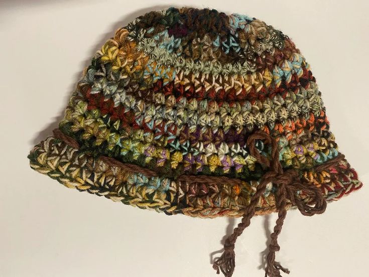 a multicolored crocheted hat is hanging on a white wall and has tassels around the brim