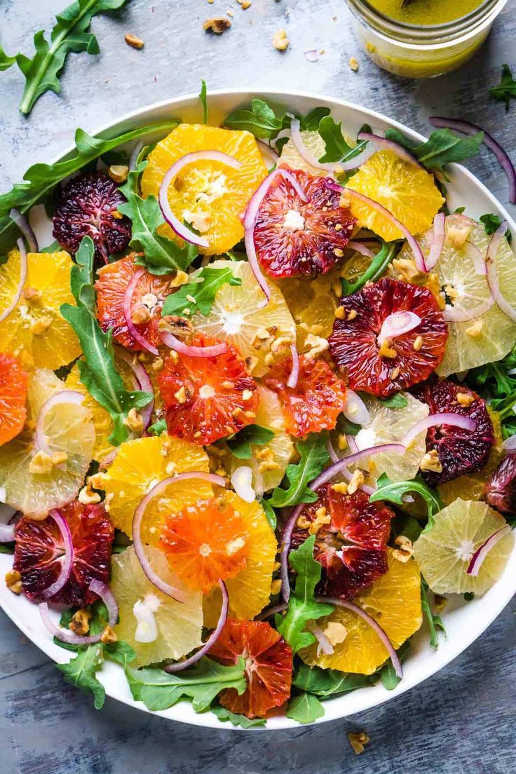 a salad with oranges, onions and spinach in a white bowl on a table