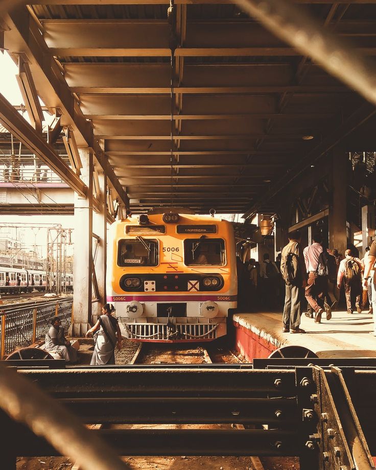 an orange and white train parked at a train station next to people walking on the platform