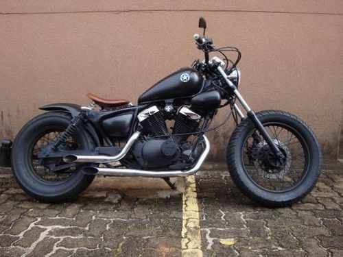 a black motorcycle parked in front of a brown wall and some bricks on the ground