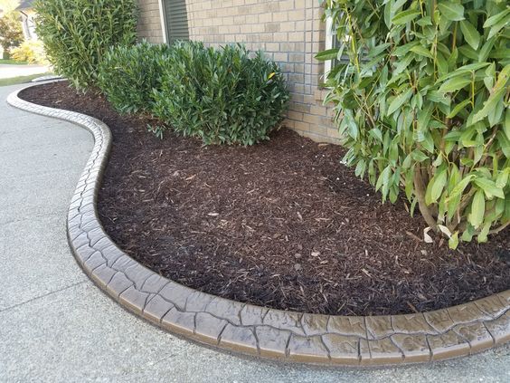 a garden bed with mulch and plants in front of a brick building