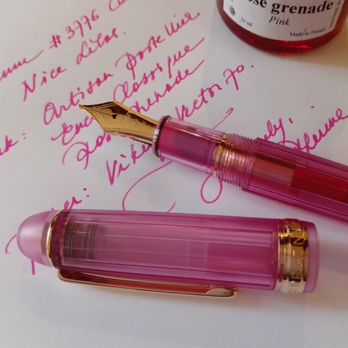 two pink pens sitting on top of a piece of paper next to a bottle of ink