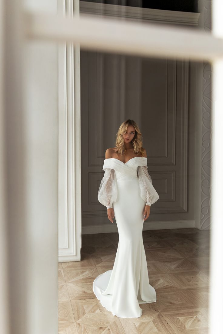 a woman in a white wedding dress looking at herself through a window with her hands on her hips