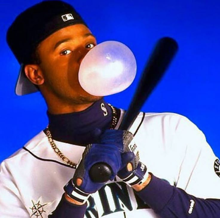 a baseball player blowing bubbles into his mouth while holding a bat in one hand and ball in the other